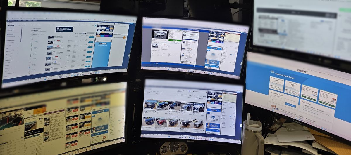 Kevin Buehler's desk: six monitors showing ADESA auction listings beside Carfax reports and vehicle pricing panels.